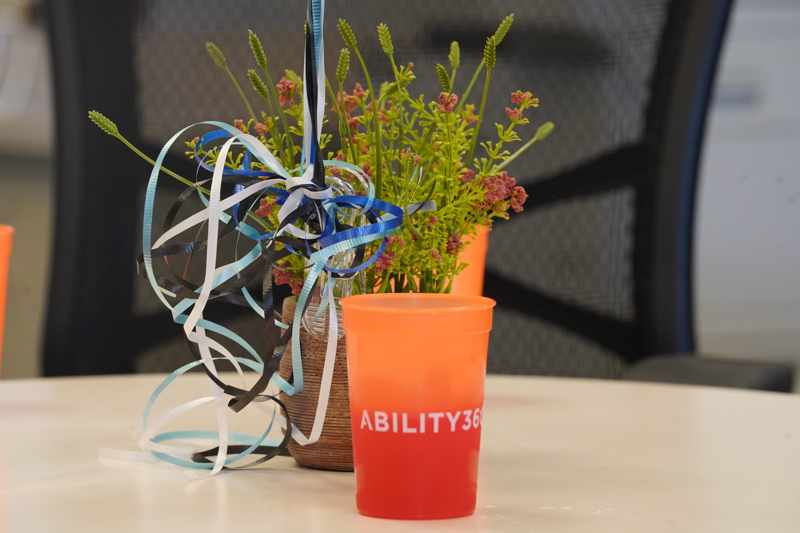 an orange cup with ability360 written on it sits on a table in front of a plan